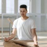 A young man meditates in a bright and serene indoor space, embodying relaxation.